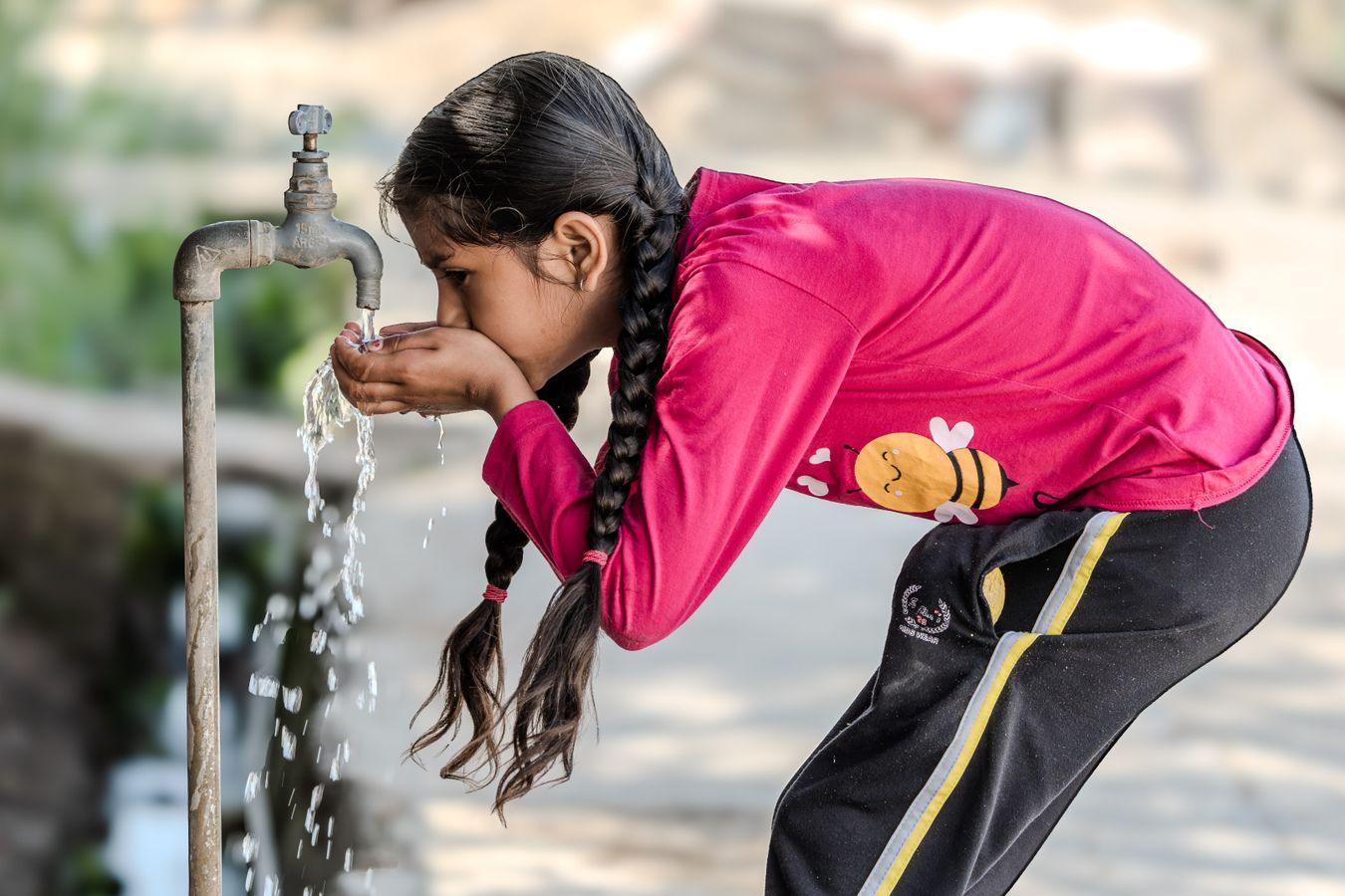 A girl drinks clean flowing water from a tap in the sunshine